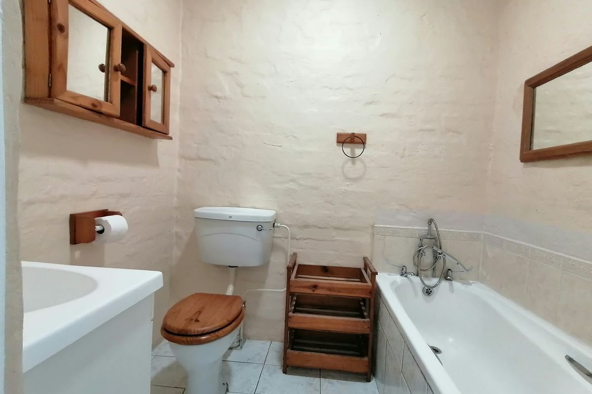 A functional bathroom featuring a bathtub, toilet, and vanity sink with textured walls and tiled flooring, offering a rustic cottage aesthetic.