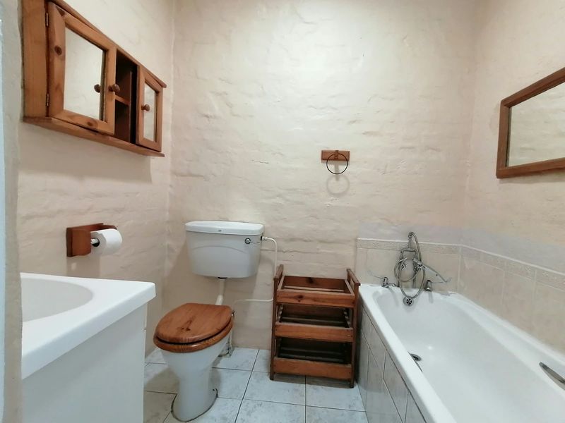 A functional bathroom featuring a bathtub, toilet, and vanity sink with textured walls and tiled flooring, offering a rustic cottage aesthetic.