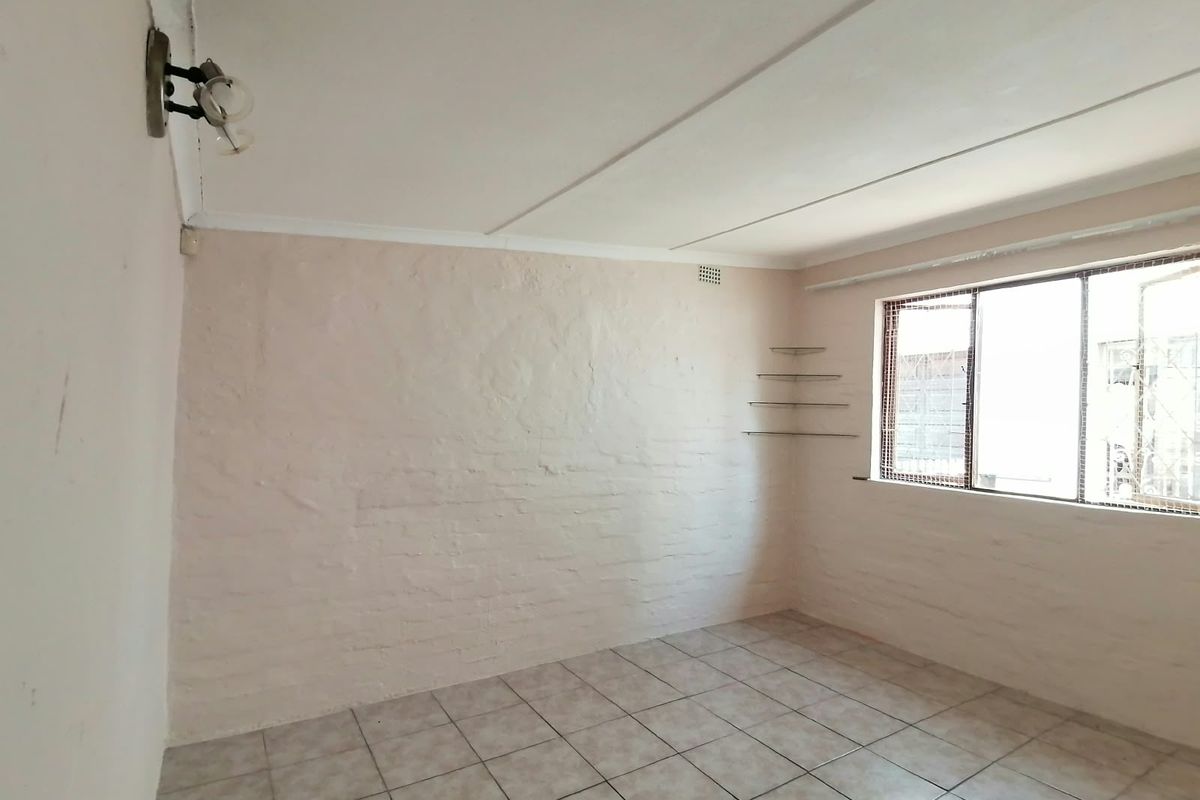 A vacant bedroom featuring tiled flooring, painted brick walls, and a window with security bars, offering a blank canvas for personalization.