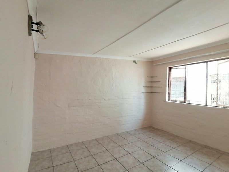 A vacant bedroom featuring tiled flooring, painted brick walls, and a window with security bars, offering a blank canvas for personalization.