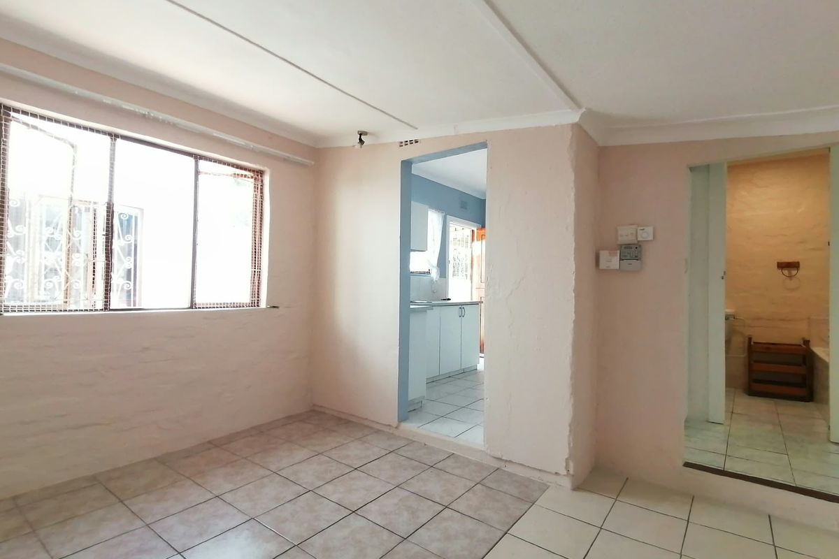 An empty living area featuring tiled flooring, coved ceilings, and direct access to the kitchen and bathroom, offering a blank canvas for renovation.