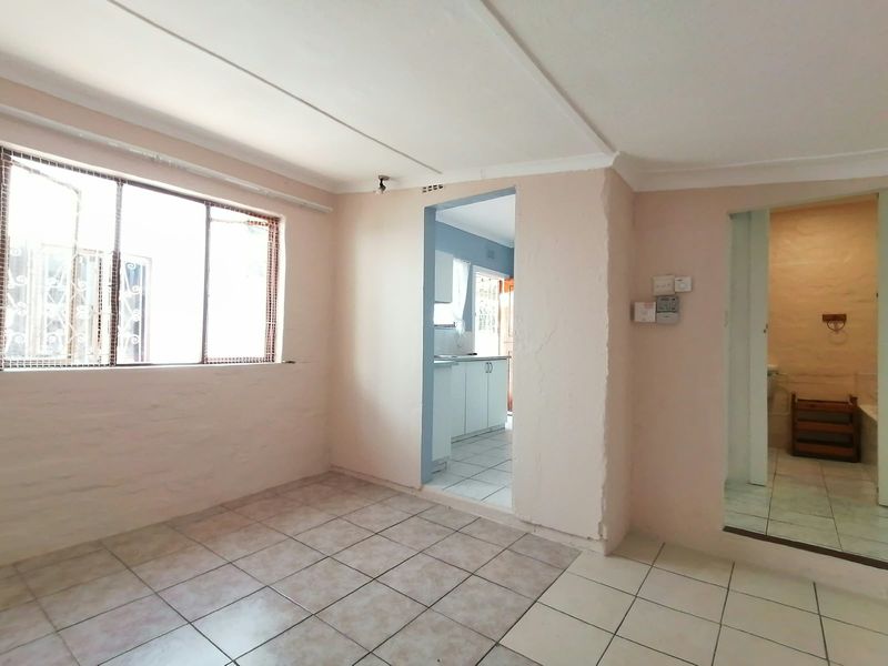 An empty living area featuring tiled flooring, coved ceilings, and direct access to the kitchen and bathroom, offering a blank canvas for renovation.