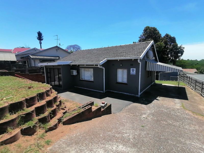 A detached house featuring a tiled roof, concrete driveway, and a retaining wall, with an attached awning over the side entrance area.
