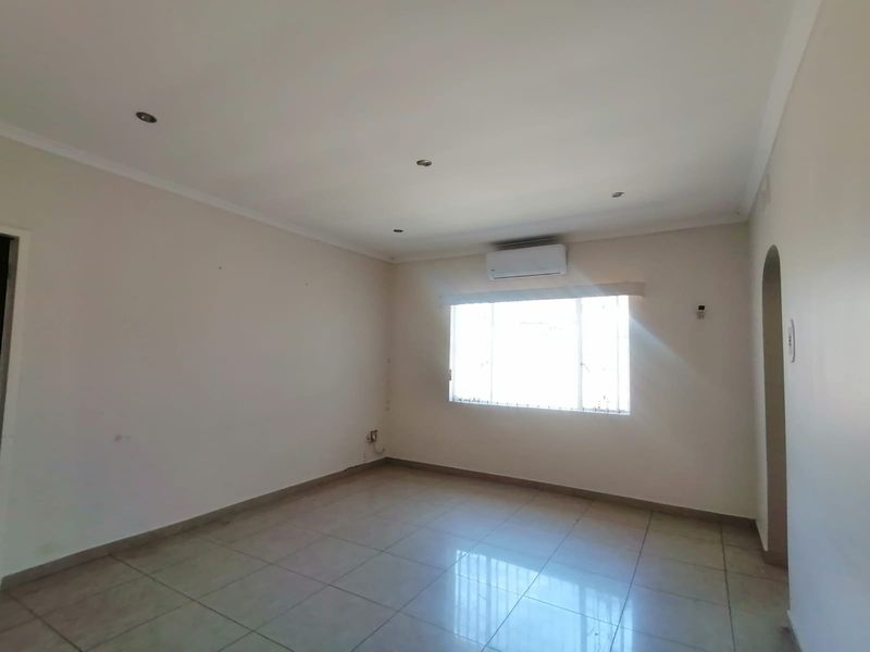 A bright, empty living room featuring tiled flooring, recessed downlights, and a wall-mounted air conditioning unit.