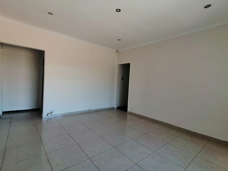 An empty, neutrally painted living area featuring tiled flooring and recessed downlighting, offering a blank canvas for interior design.