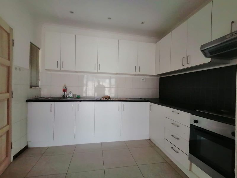 A clean, functional kitchen featuring white cabinetry, dark countertops, tiled backsplash, and integrated oven with extractor fan.