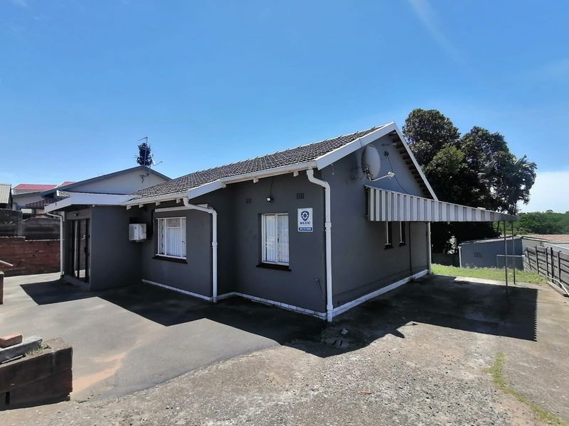 Rear view of the property featuring a tiled roof, asphalt driveway, and a fixed side awning.