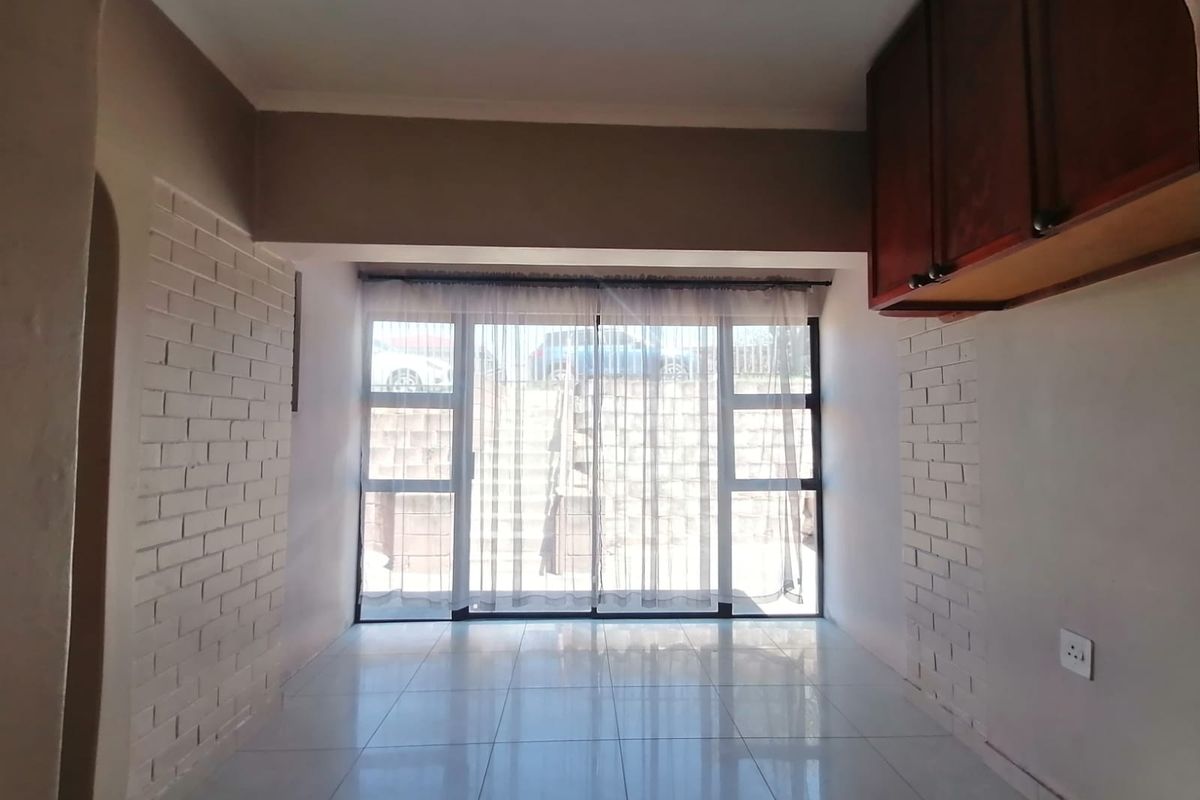 An empty living area featuring tiled floors, exposed brick accent walls, and a large sliding glass door providing natural light and access to the exterior.