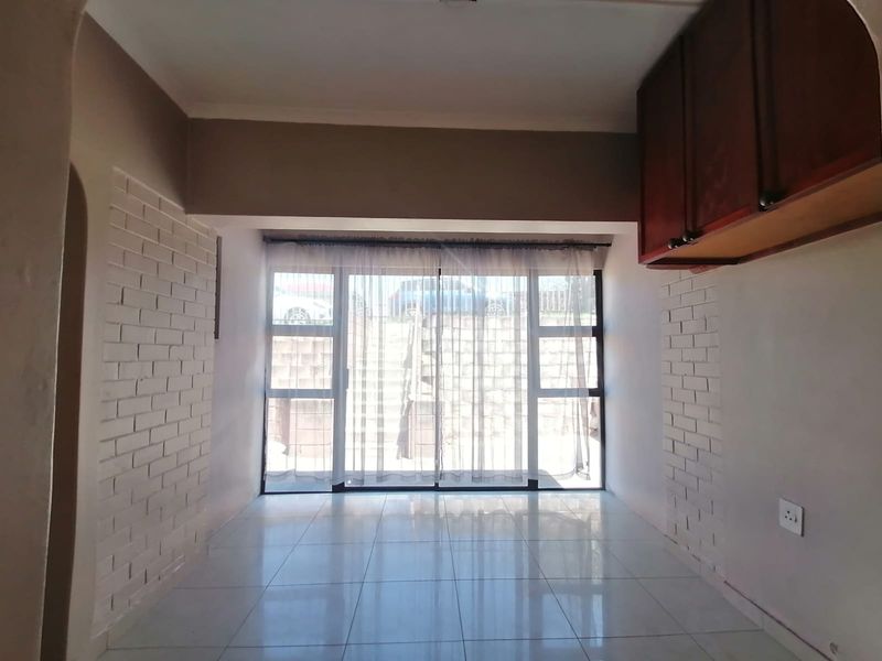 An empty living area featuring tiled floors, exposed brick accent walls, and a large sliding glass door providing natural light and access to the exterior.