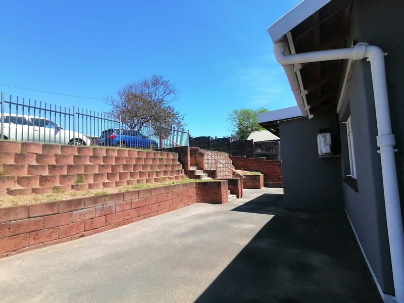 Rear exterior area featuring concrete paving, a tiered brick retaining wall, and steel perimeter fencing.