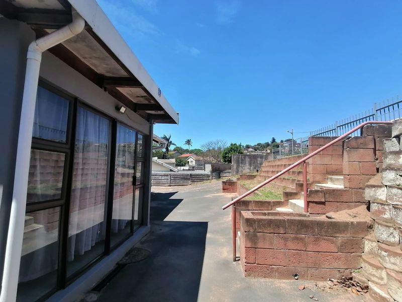 Rear exterior view featuring a paved walkway, sliding glass doors, and tiered brick retaining walls with a metal handrail.