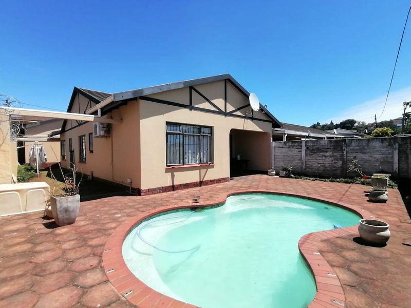 Rear exterior view of the townhouse featuring a swimming pool, paved patio area, and perimeter boundary wall.