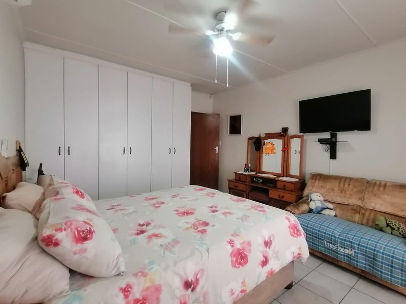 A functional bedroom featuring built-in white cupboards, a ceiling fan, and tiled flooring, offering a practical and comfortable living space.