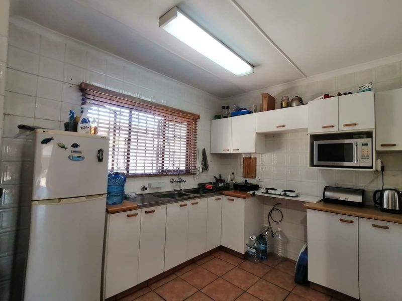 A functional kitchen featuring white cabinetry, tiled backsplash, stainless steel sink, and tiled flooring, offering a practical layout with ample storage space.