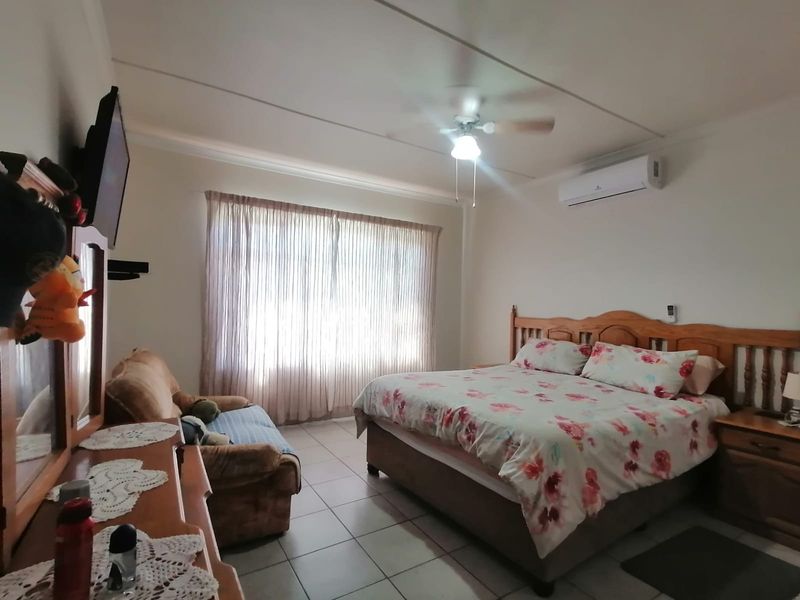 Spacious bedroom featuring tiled flooring, a ceiling fan, and a wall-mounted split-system air conditioner for climate control.