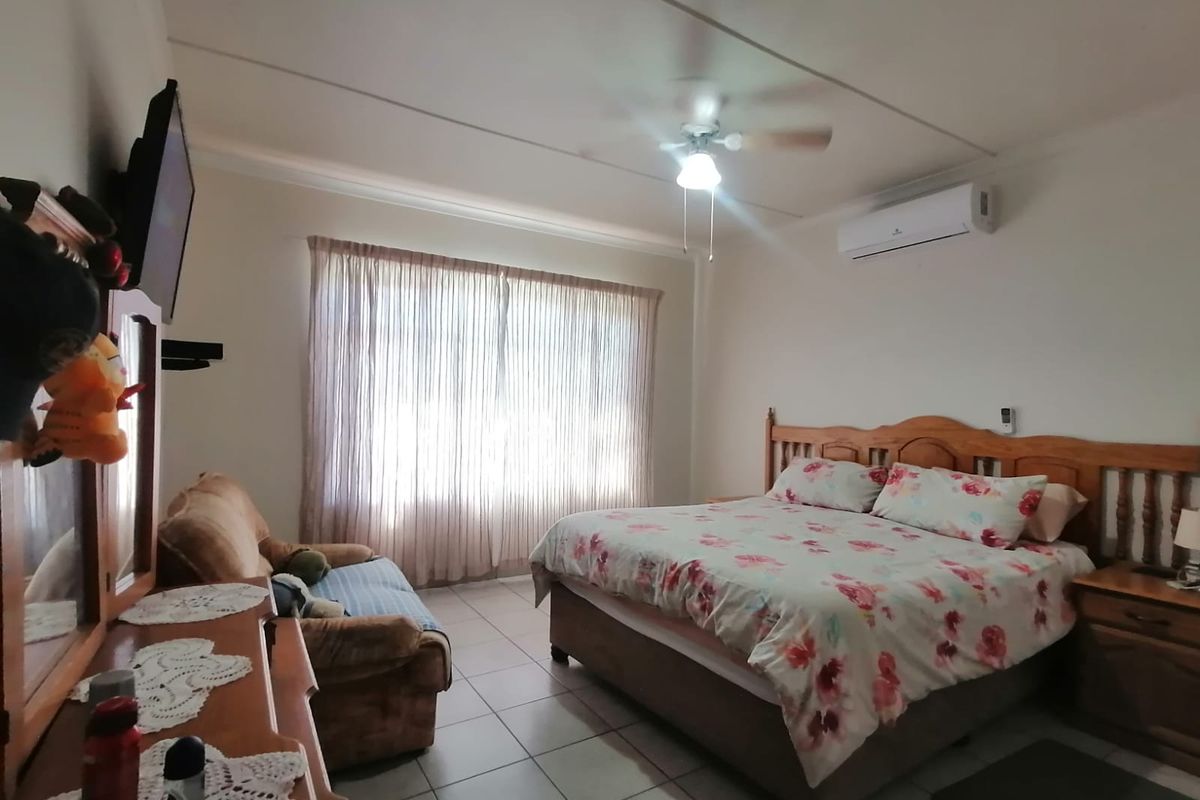 Spacious bedroom featuring tiled flooring, a ceiling fan, and a wall-mounted split-system air conditioner for climate control.