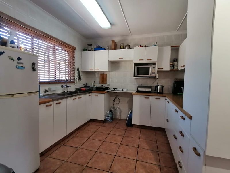 A functional kitchen featuring white cabinetry, tiled backsplash, tiled flooring, and a double sink, offering a practical layout for daily meal preparation.