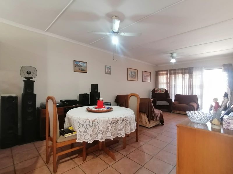 Spacious open-plan living and dining area featuring tiled flooring, ceiling fans, and natural light through a sliding glass door.
