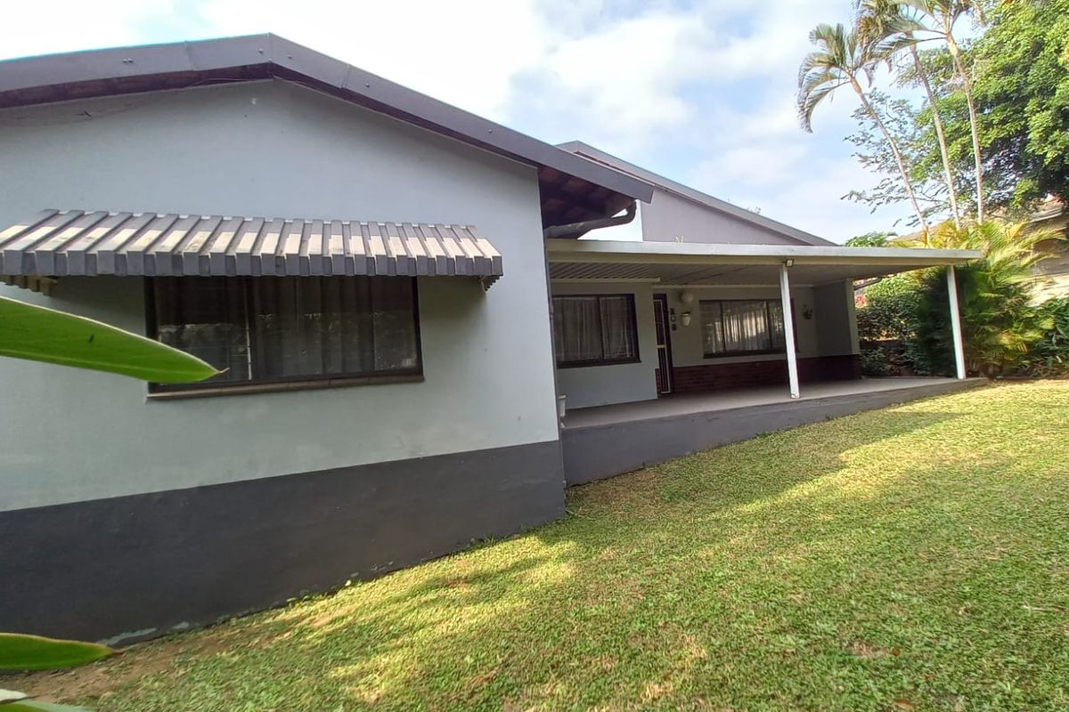Rear view of the house featuring a covered patio area, metal window awnings, and a spacious garden lawn.
