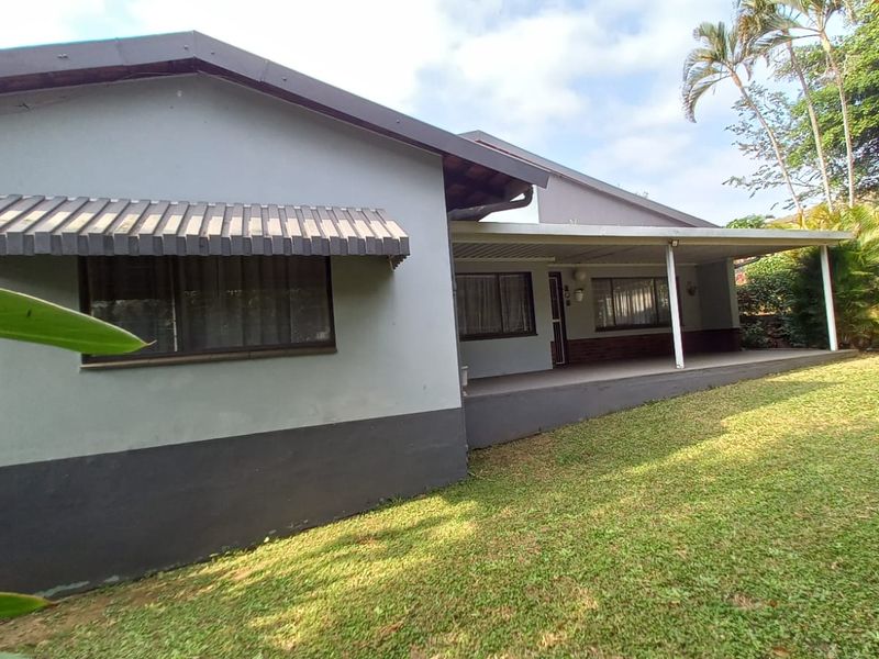 Rear view of the house featuring a covered patio area, metal window awnings, and a spacious garden lawn.