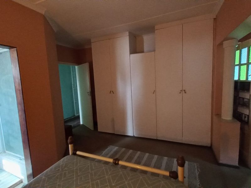Bedroom featuring built-in cupboards and an en-suite shower area, offering potential for modernization through updated finishes and lighting.