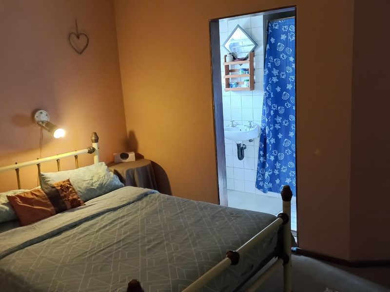 A bedroom featuring warm-toned walls and an adjoining en-suite bathroom with a pedestal basin.