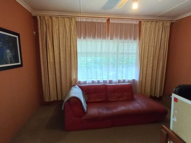 A living room featuring terracotta-toned walls, a large window with floor-to-ceiling curtains, and a ceiling fan.