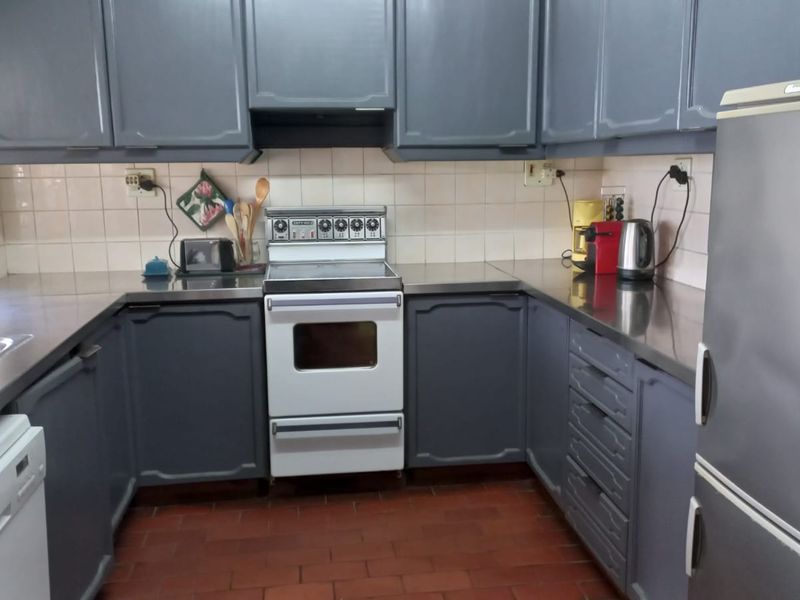 A functional kitchen featuring grey cabinetry, stainless steel countertops, a freestanding oven, and terracotta tile flooring with a classic layout.