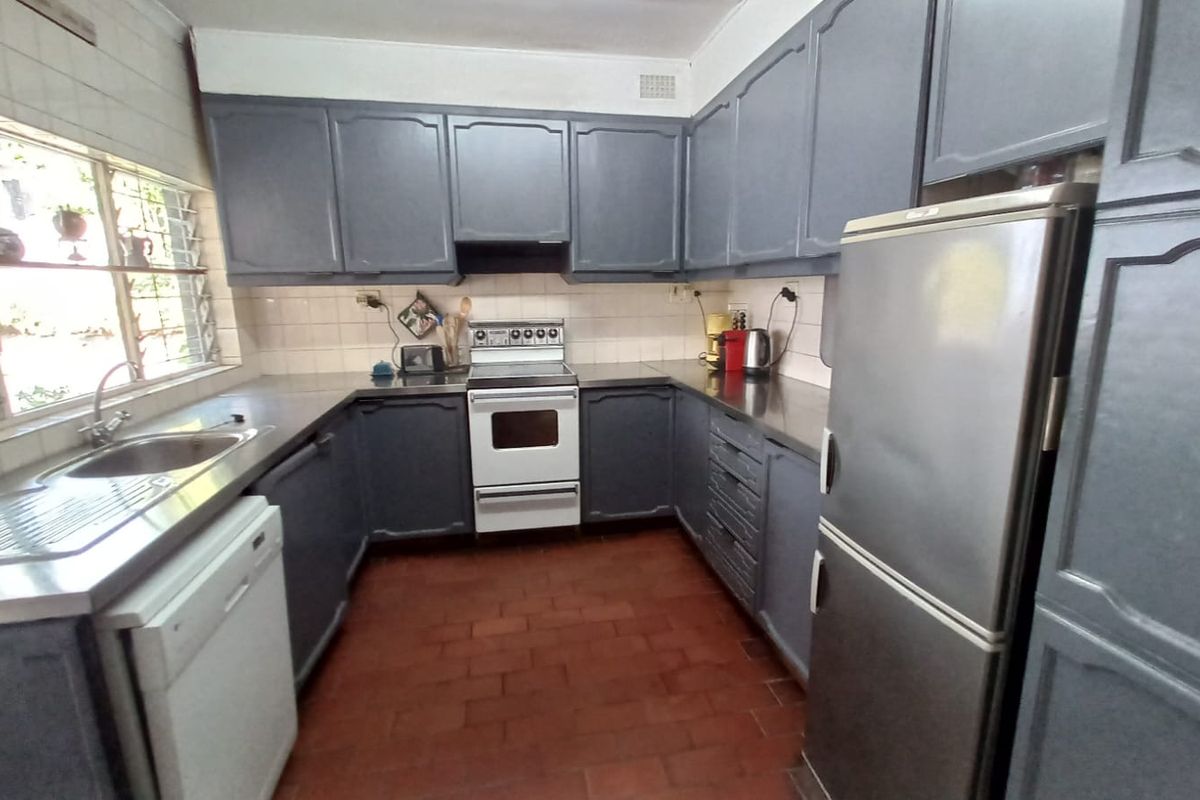 A functional kitchen featuring dark painted cabinetry, stainless steel sink, tiled backsplash, and durable terracotta flooring, offering a classic layout with ample storage space.