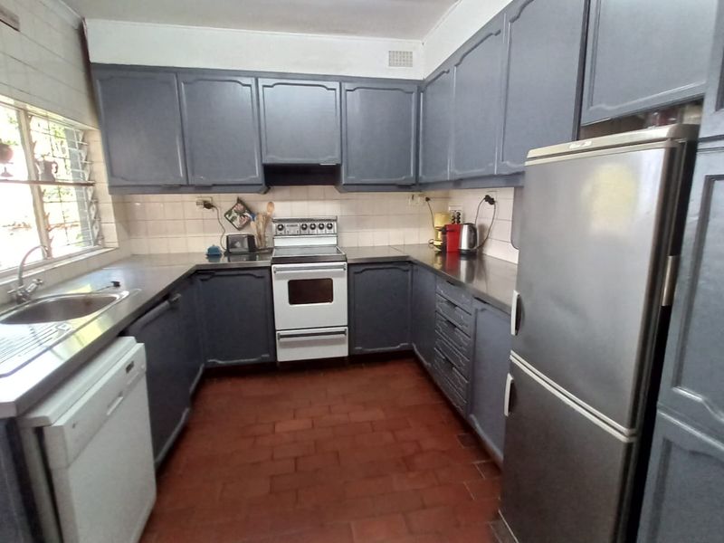 A functional kitchen featuring dark painted cabinetry, stainless steel sink, tiled backsplash, and durable terracotta flooring, offering a classic layout with ample storage space.