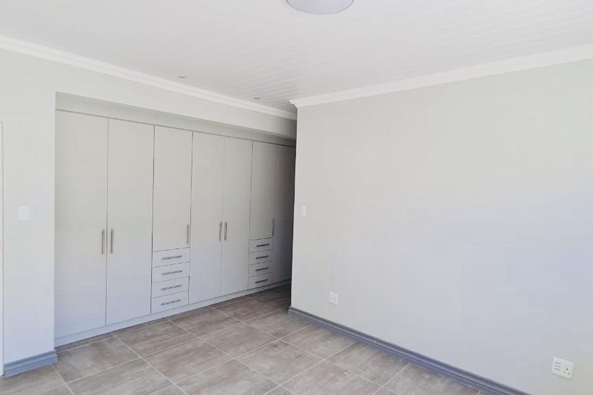 A bright bedroom featuring neutral tiled flooring, built-in cabinetry with integrated drawers, and a clean, modern aesthetic.