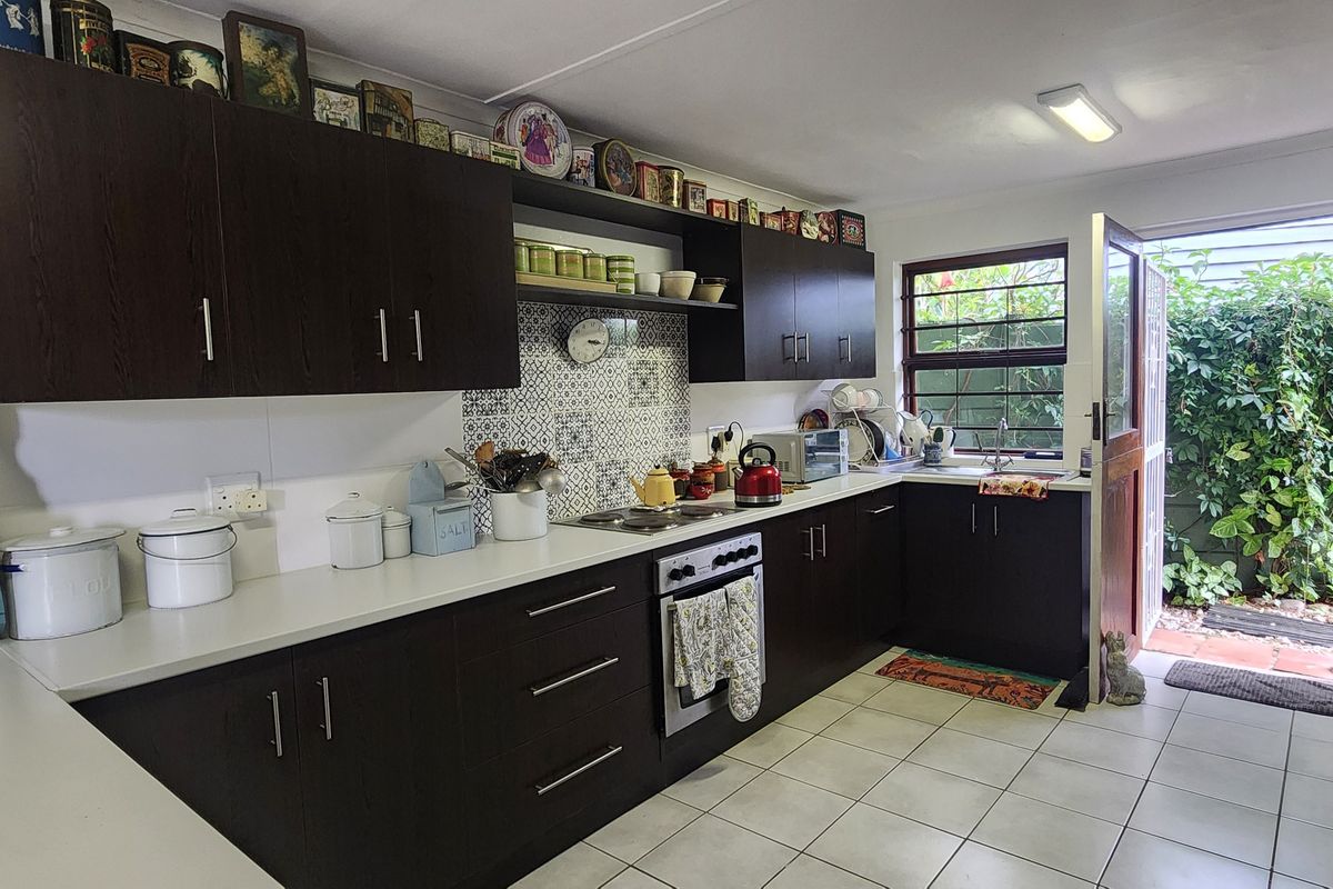 A functional kitchen featuring dark wood cabinetry, a patterned tile backsplash, built-in oven, and direct access to a private rear garden area.