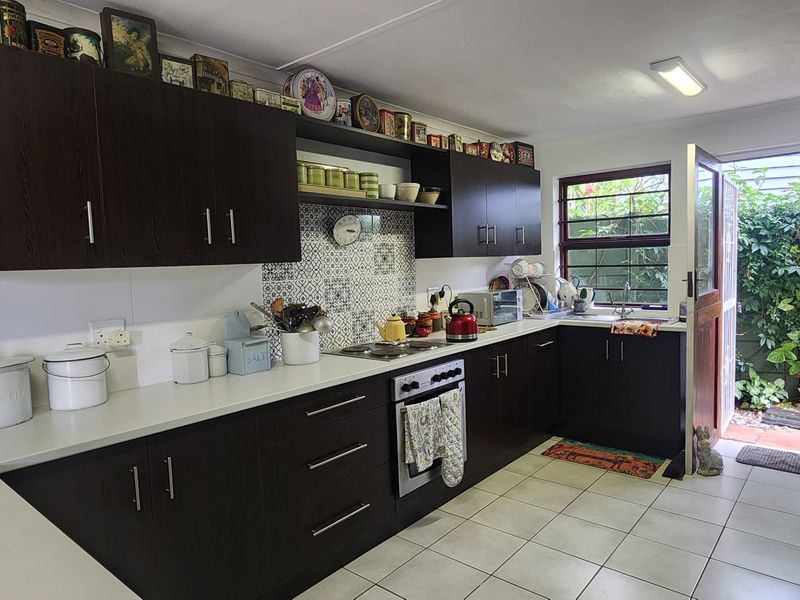 A functional kitchen featuring dark wood cabinetry, a patterned tile backsplash, built-in oven, and direct access to a private rear garden area.