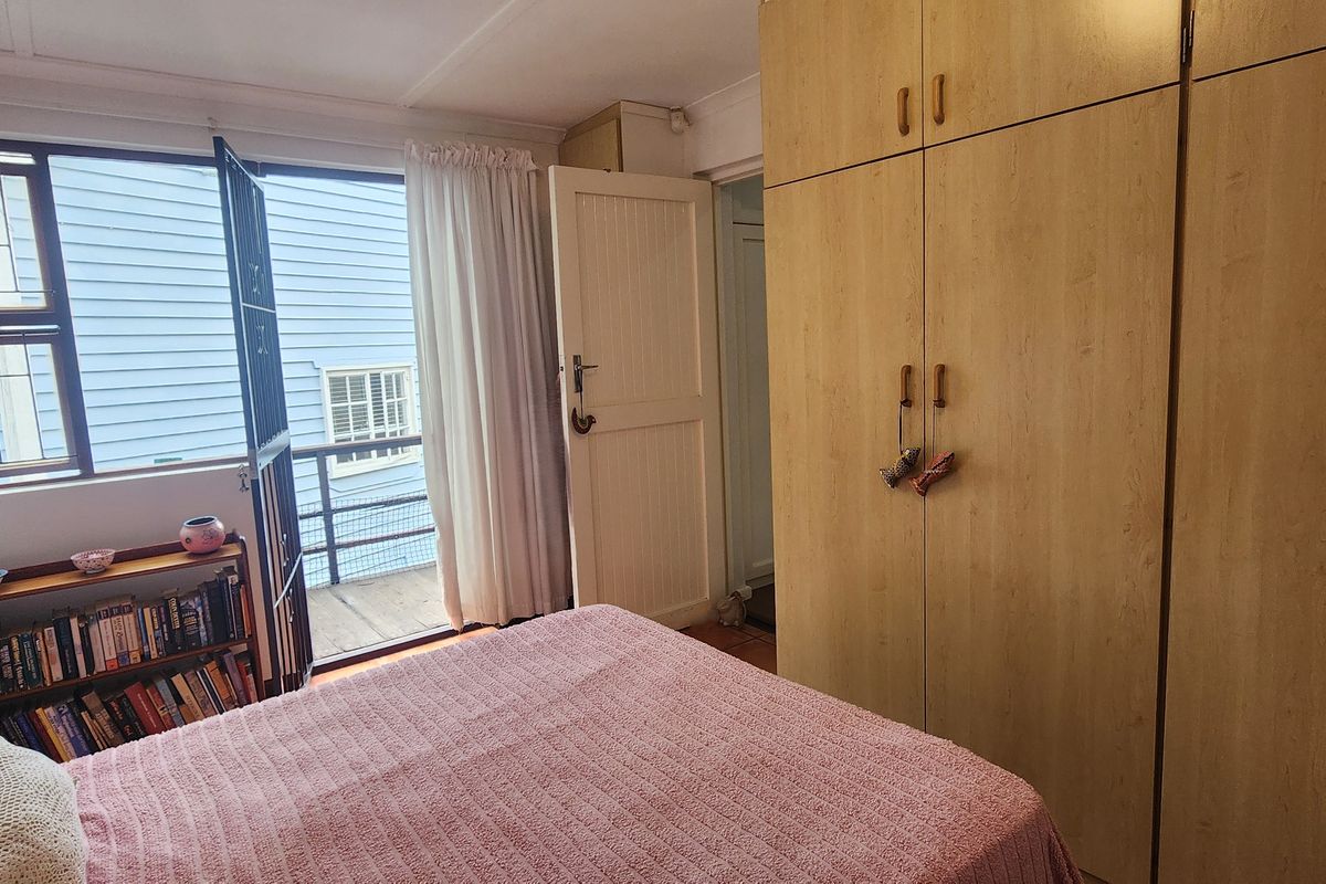 A bedroom featuring built-in wooden cupboards, a security gate leading to a small balcony, and natural light through a large window.