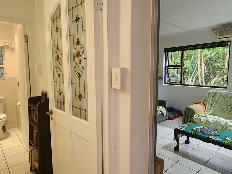 An open-plan living area adjacent to a bathroom, featuring tiled floors, stained glass detailing, and a wall-mounted air conditioning unit.