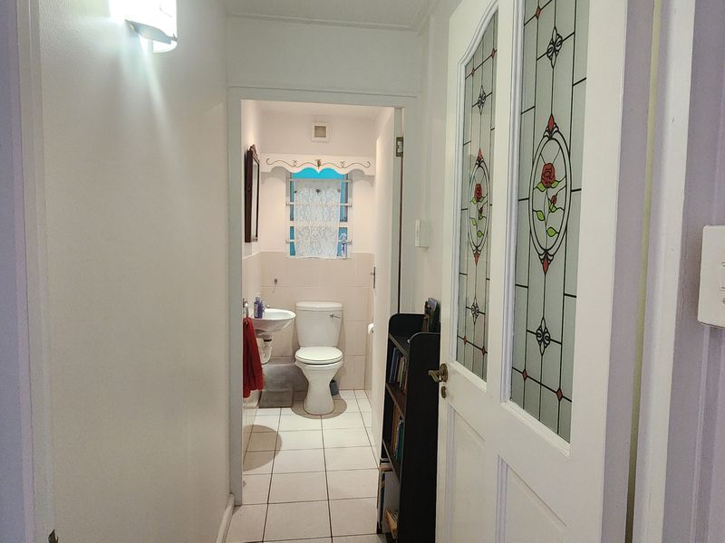 A view from a hallway looking into a small bathroom featuring tiled floors, a pedestal basin, and a toilet, with a decorative leaded glass door.