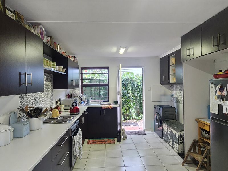 A functional kitchen featuring dark cabinetry, white countertops, tiled backsplash, and direct access to the rear exterior area.