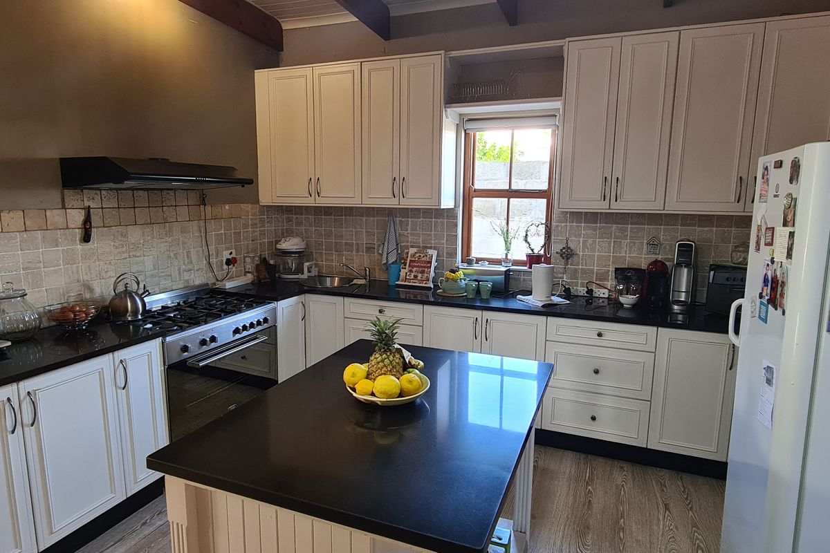 A well-appointed kitchen featuring white cabinetry, dark granite countertops, a central island, and a built-in gas hob with an extractor fan.