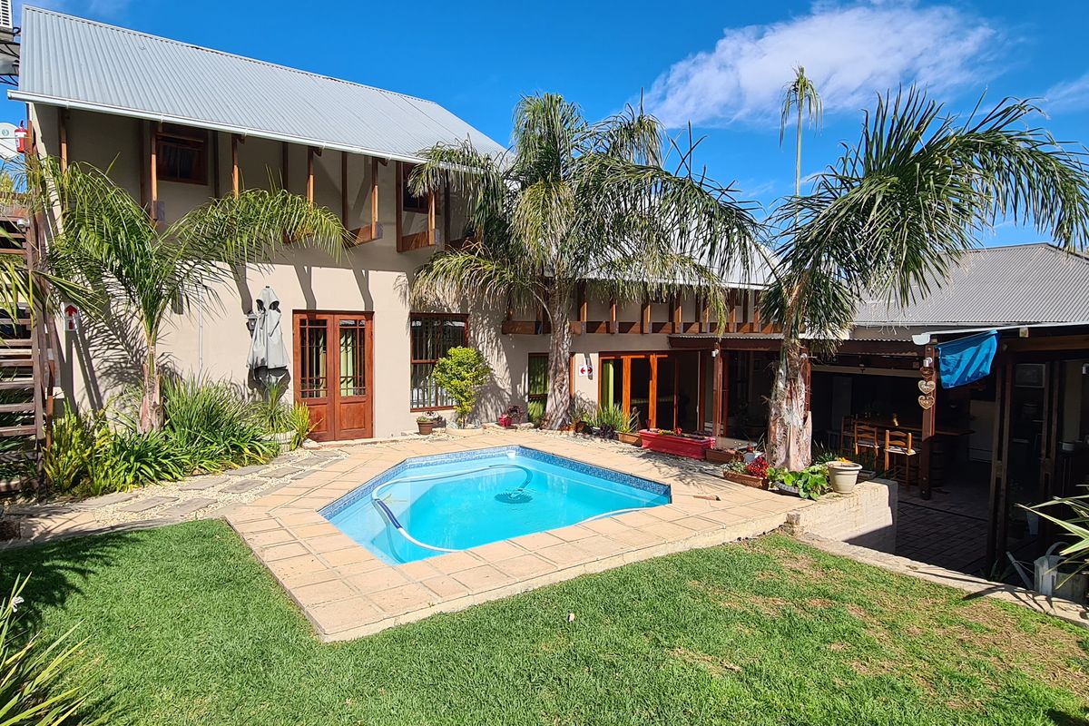 Rear view of the property featuring a swimming pool, landscaped garden, covered patio area, and multi-level exterior structure with metal roofing.