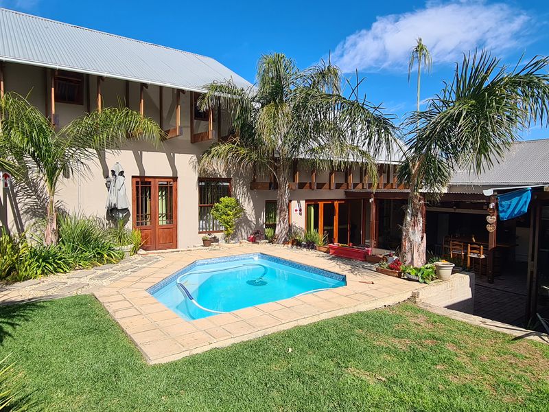 Rear view of the property featuring a swimming pool, landscaped garden, covered patio area, and multi-level exterior structure with metal roofing.
