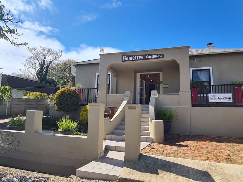 Front elevation of the Flametree Guesthouse featuring a covered entrance porch, concrete stairs, and a paved driveway area.