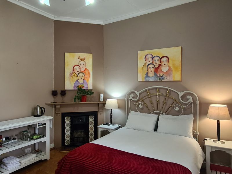 A cozy bedroom featuring a built-in fireplace with a decorative mantel, hardwood flooring, and large windows with light-filtering curtains.