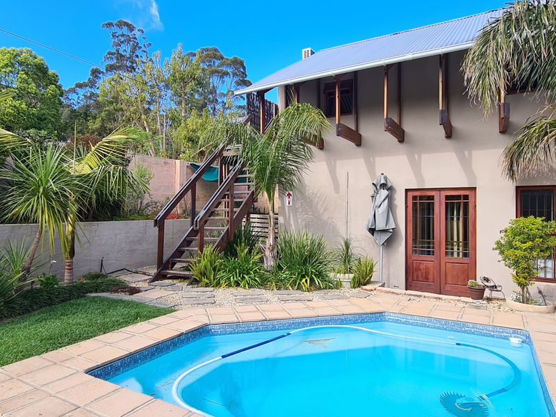 Rear exterior view featuring a swimming pool with paved surround, landscaped garden, and an external timber staircase leading to the upper level.