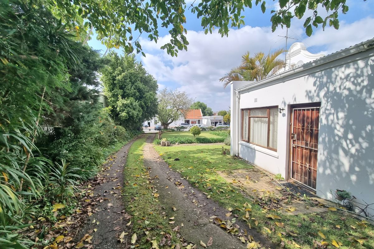 A view of the property's side garden and driveway, featuring established landscaping and access to the side entrance of the house.