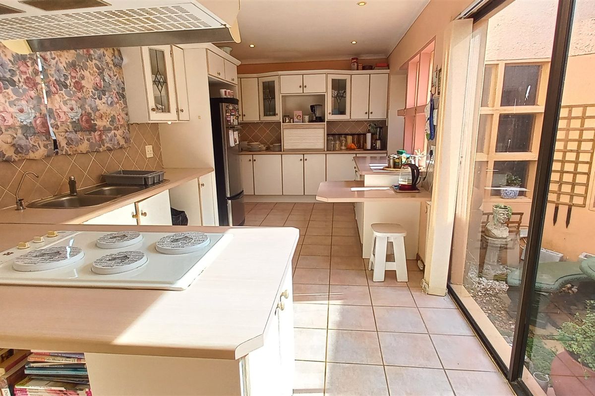 Spacious kitchen featuring white cabinetry, integrated hob, and tiled flooring, with large sliding glass doors providing direct access to an internal courtyard.
