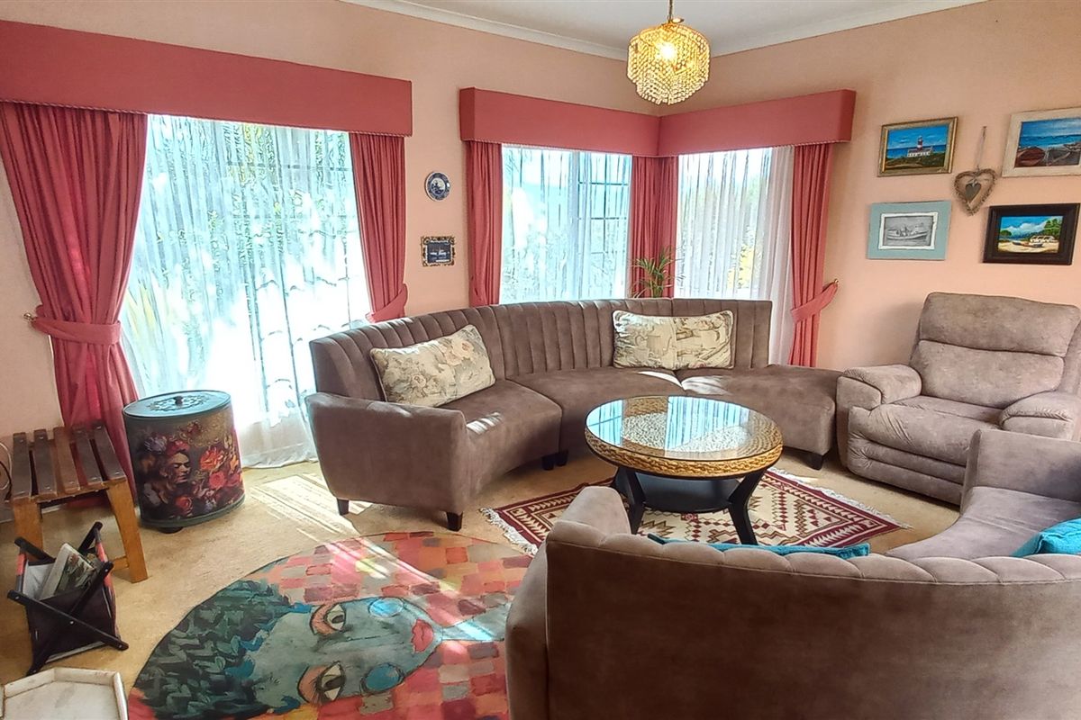 A spacious living room featuring large windows with built-in pelmets, carpeted flooring, and a classic chandelier, offering a comfortable and traditional living space.