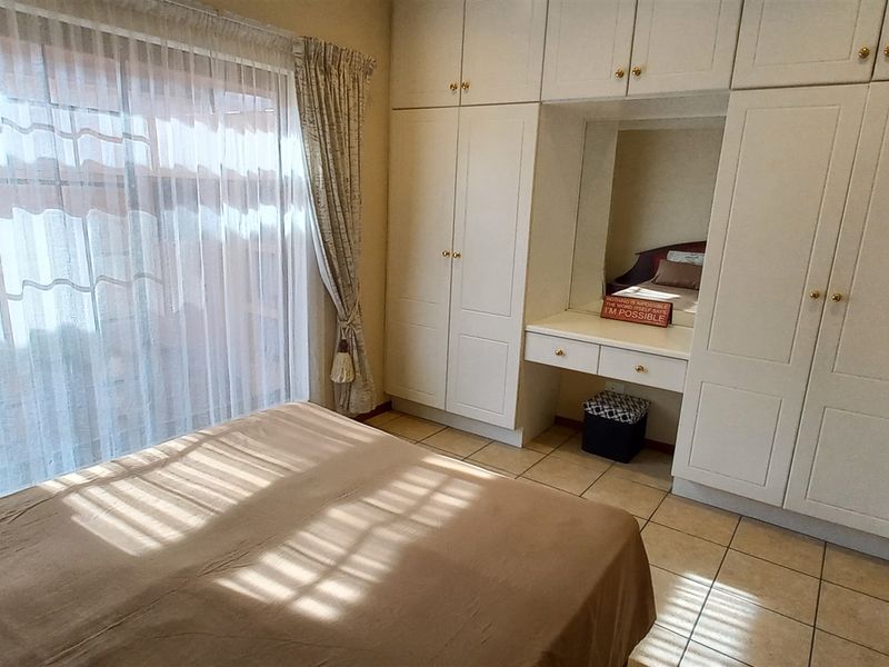 A bedroom featuring built-in white cabinetry with an integrated vanity and tiled flooring, illuminated by natural light through a large window.