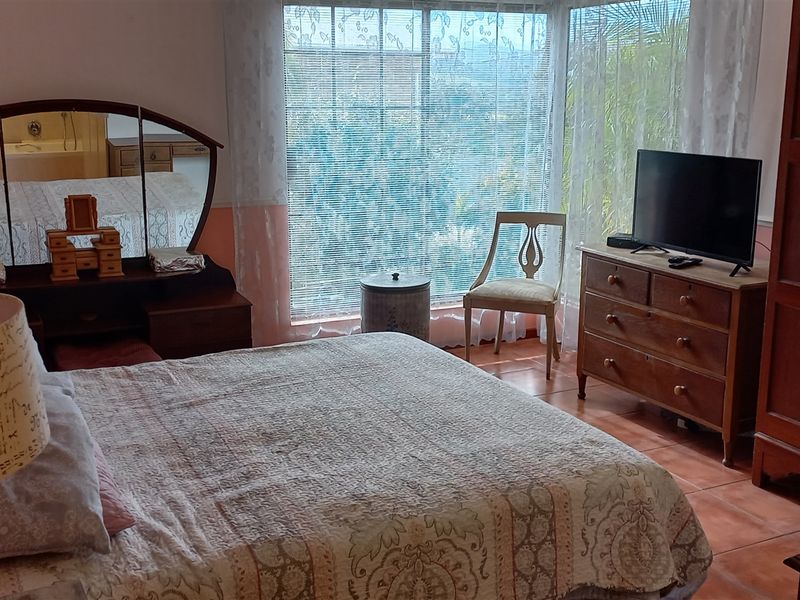 A bedroom featuring large windows with natural light, tiled flooring, and a neutral wall finish.