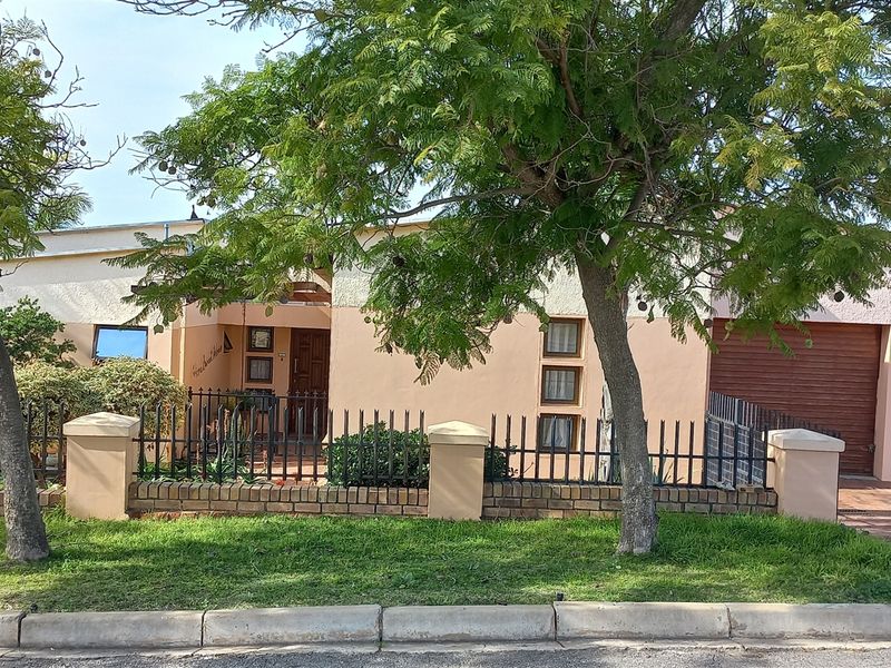 Front elevation of a single-story house featuring a paved driveway, double garage, and a secure boundary wall with metal fencing.