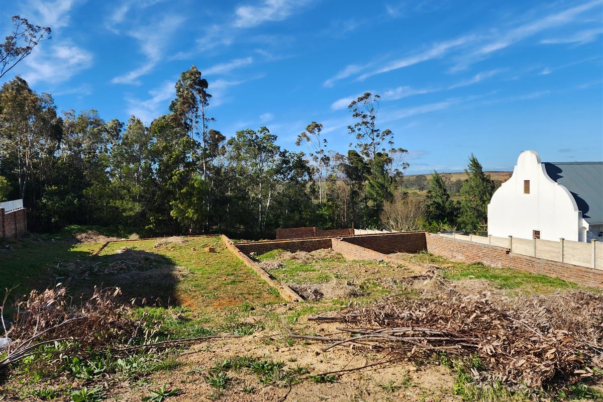 A vacant residential plot featuring existing brick foundation walls, surrounded by established trees and neighboring property boundaries.